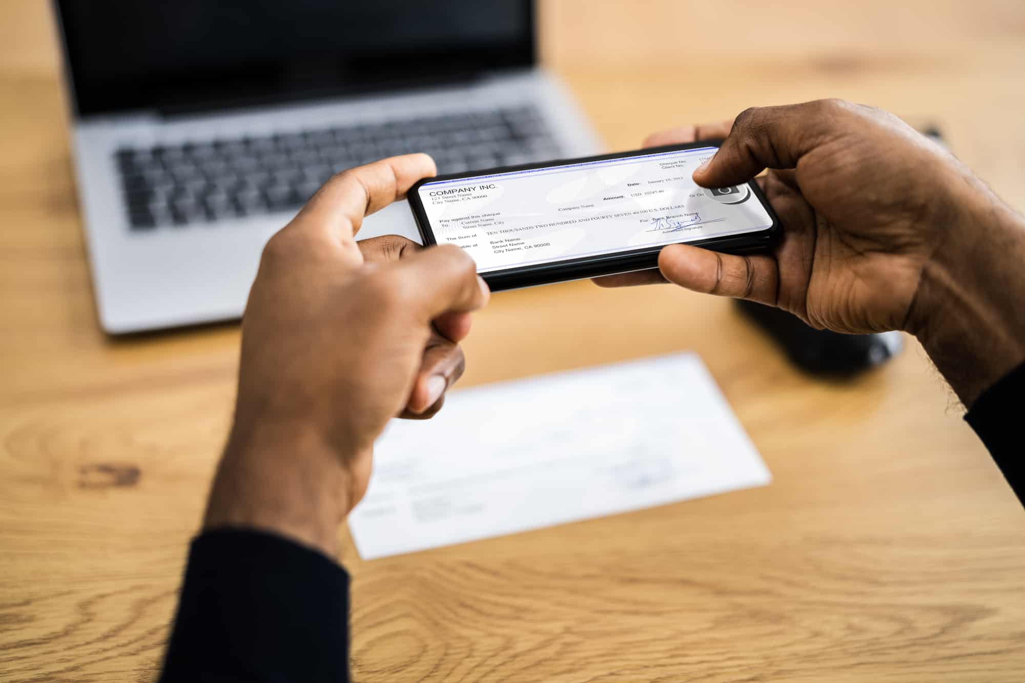How to pay yourself-Black man writing a check from his business account to mobile deposit into a personal bank account.
